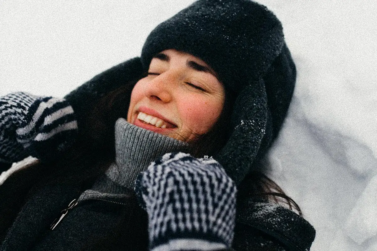 Laughing woman in a hat and gloves lying in the snow