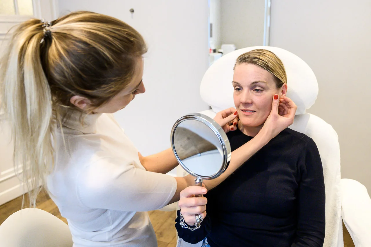 Woman in a white top holding a hand mirror up to a client in the treatment chair