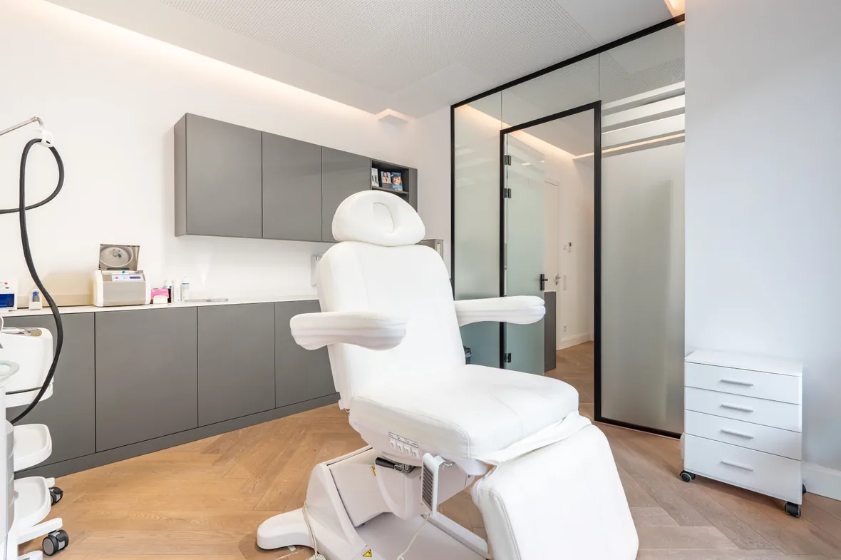 Treatment room interior:
Modern cosmetic treatment room with an adjustable white chair, gray cabinets and a glass entrance door.