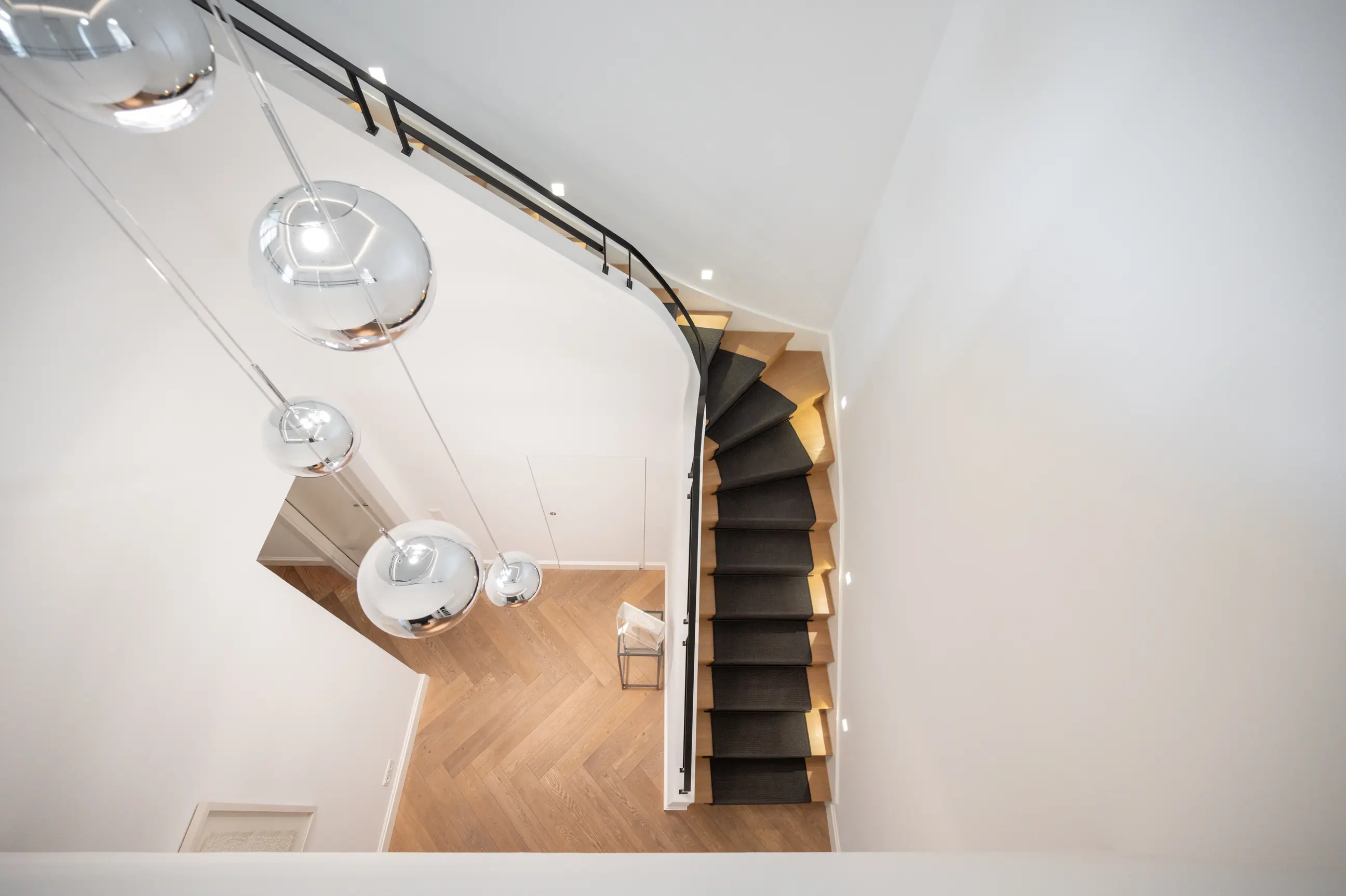 Interior photo of the practice: modern wooden staircase with a dark carpet runner and round pendant lights, seen from above.